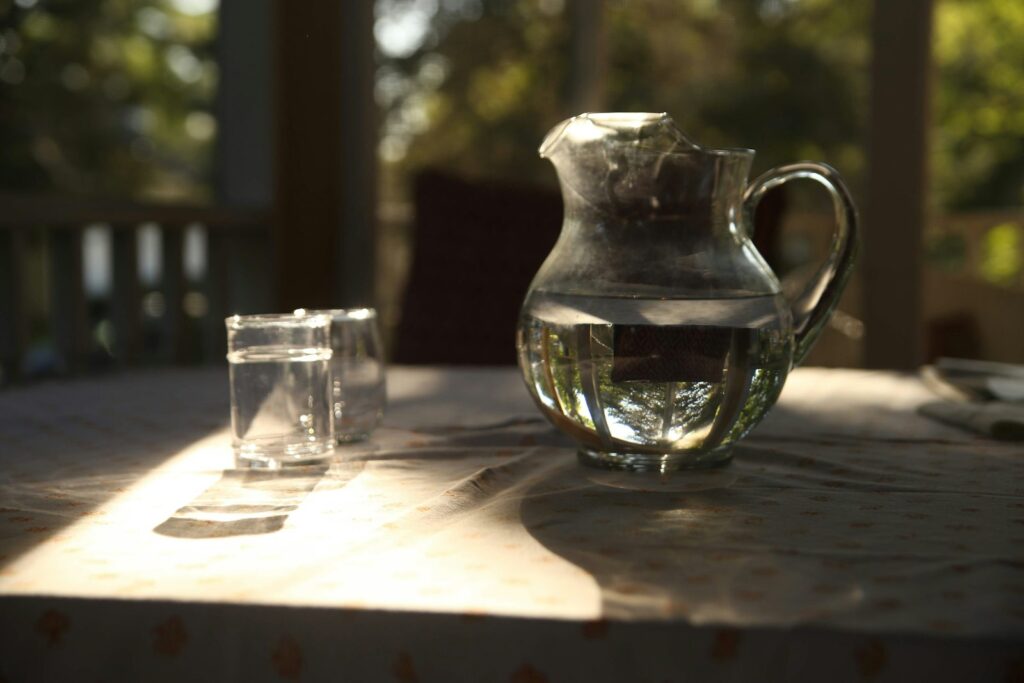 Een glazen kan met water naast een glas op tafel