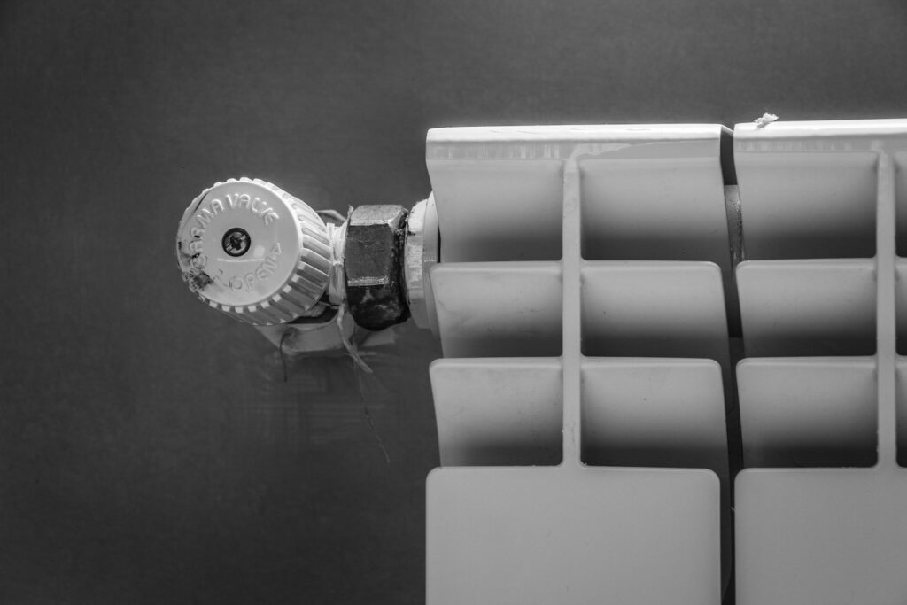 Hand draait aan de thermostaatkraan van een radiator in een woonkamer