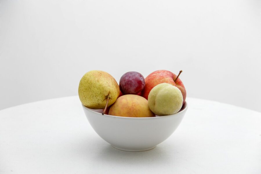 Een fruitschaal met rijpe bananen en appels, waar fruitvliegjes op afkomen
